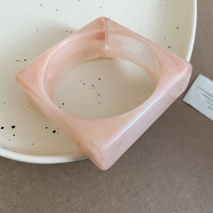 Detail of a square acrylic bangle in pink marble texture on a beige ceramic plate