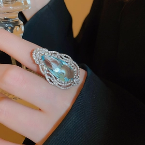 Close-up of a blue water drop gemstone ring with pavé diamond halo on female hand