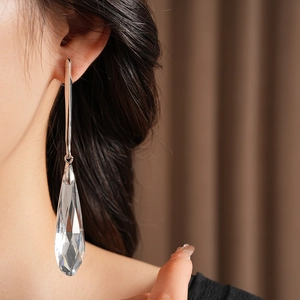 Close-up of silver long drop earring with faceted clear glass teardrop worn by a model