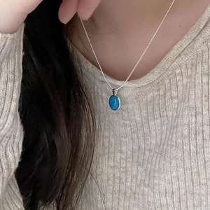 Detail showing an oval turquoise pendant on a delicate silver chain worn by a model