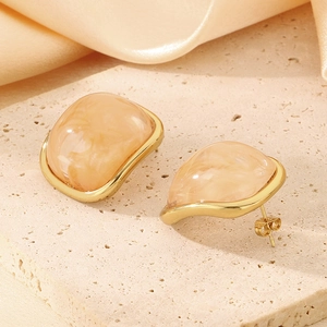 Détail de boucles d'oreilles carrées en or et résine sur un fond de pierre beige élégant