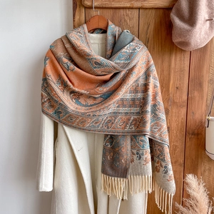 Close-up of orange paisley jacquard shawl with fringe on a white coat background
