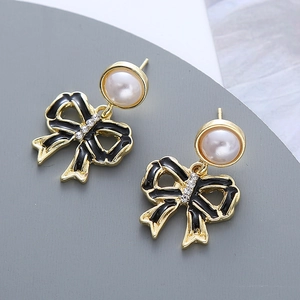 Détail de boucles d'oreilles papillon dorées avec émail noir, perles et zircons brillants