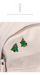 Detailed view of two green enamel Christmas tree brooches pinned on a canvas bag