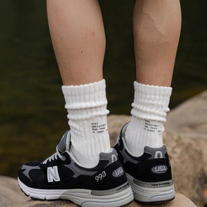 Classic black New Balance 993 sneakers with white thick cotton crew socks on nature rocks