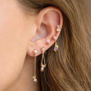 Close-up of gold ear studs set with pink heart and opal bear charms for multi-piercing