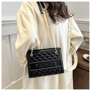 Close-up of quilted black PU shoulder bag with gold chain strap on a beige coat