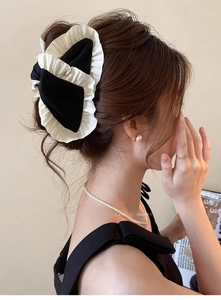 Detail of a large black and white pleated fabric bow hair clip on model's hair