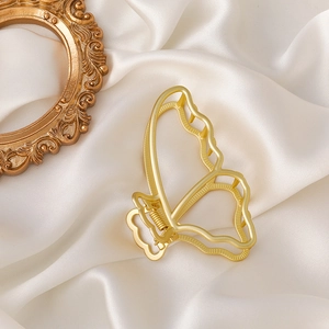 Detail van een grote gouden mat vlinder haarclip op zachte witte zijden stof