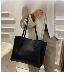Minimalist black tote bag in soft grainy leather texture shown in a modern interior setting