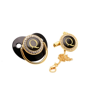 Close-up of black baby pacifier and clip with gold letter Q and sparkling rhinestones
