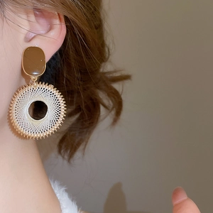 Detail of bohemian woven hoop earring with brown enamel and cream cord on model