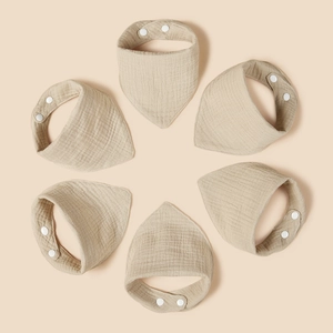 Detailed view of six beige cotton gauze baby bibs with soft crinkled texture and snaps