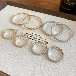 Flat lay of gold and silver textured hoop earrings in large and small sizes on fabric