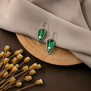 Detail of green leaf drop earrings with white pearls on a rustic wood tray