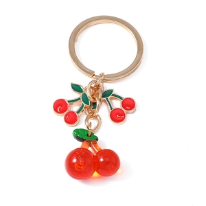 Golden cherry keychain with vibrant red resin fruit and green leaf pendants on white background