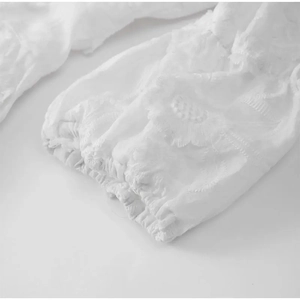 Gros plan d'une robe blanche montrant de la broderie et des textures plissées délicates