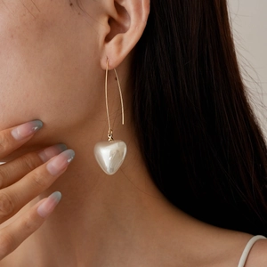 Close-up of elegant gold long hook earrings with white 3D heart-shaped pearl pendant