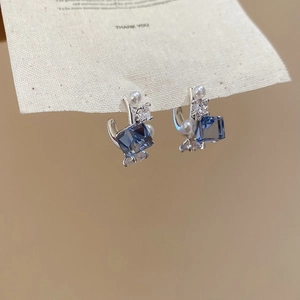 Detailed close-up of blue square zircon and white pearl bow earrings on a gift card