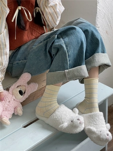 Close-up of cute white bear plush slippers worn with yellow striped socks on a wooden stool