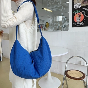 Blue pleated dumpling crossbody bag shown in a stylish minimalist lifestyle setting