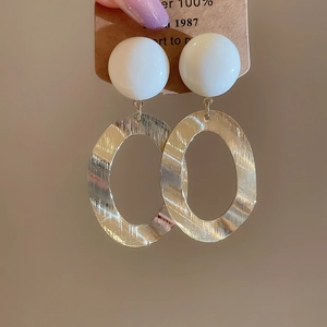 Detail of brushed gold oval drop earrings with white resin studs on kraft card