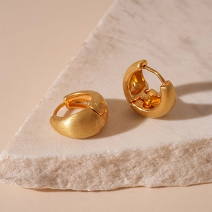 Minimalist thick gold hoop earrings with a brushed metal finish on a textured stone