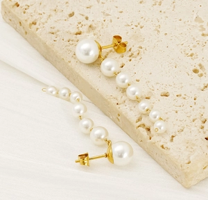 Close-up of elegant long pearl tassel earrings with gold finish on a textured stone base