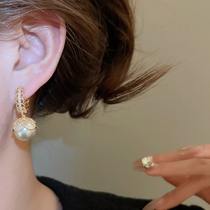 Detail of gold-plated lace earring with zircon inlay and large lustrous white pearl