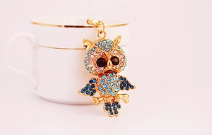 Detailed view of an owl keychain with blue and pink rhinestones leaning on a ceramic cup