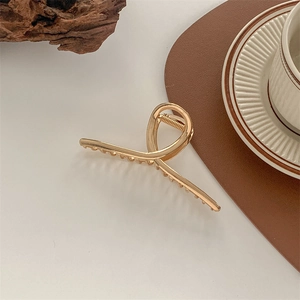 Close-up of a large golden metal hair claw clip with a sleek twisted design on a white table