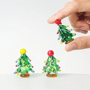 Macro shot of three miniature green glass Christmas trees with colorful ornaments on a fingertip