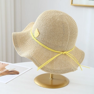 Detail of a beige woven straw sun hat featuring a wavy wide brim and yellow tulip accent