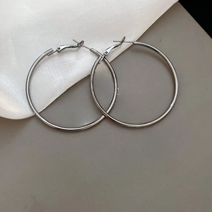 Macro detail of large silver metallic hoop earrings on beige silk fabric backdrop
