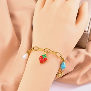 Golden chain bracelet with red strawberry, butterfly, and pearl charms on hand model