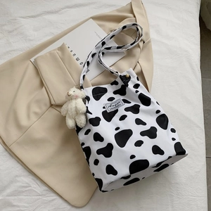 Close-up of cow print canvas tote bag with a white plush bear charm on white bedding