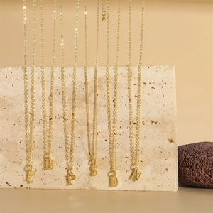 Polished gold initial letter pendants hanging on thin chains over natural stone