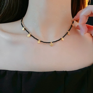 Gros plan d'un collier de perles noires avec pendentifs disques dorés sur le cou