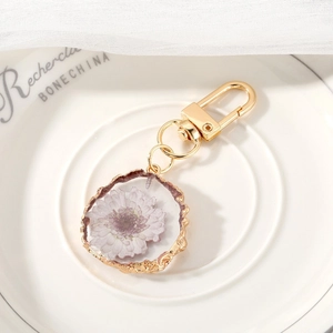 Macro detail of a resin keychain with real purple flower and wavy gold metal frame