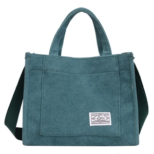 Deep teal corduroy crossbody bag with front pocket and white label in studio lighting