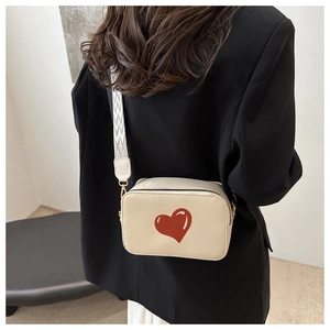 Detail of cream square crossbody bag with red heart and geometric woven strap
