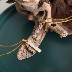Elegant gold necklace with rectangular white zircon pendant draped on natural wood
