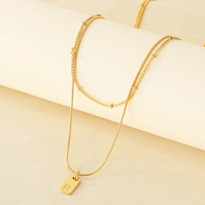 Detail einer zweilagigen goldenen Schlangenkette mit einem gravierten Buchstaben R Anhänger