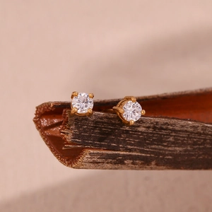 Macro shot of gold stud earrings with round-cut clear gemstones on a rustic wood stand