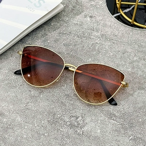 Detail of cat eye sunglasses with gold metal frame and gradient brown lenses on stone