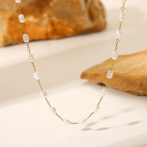 Detailed close-up of 18K gold plated chain with small white pearls on stone surface