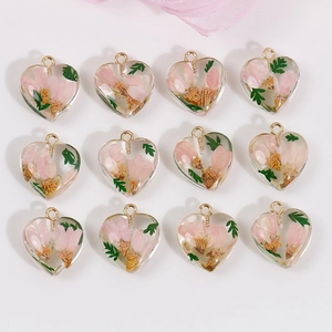 Flat lay of twelve heart-shaped resin charms with pink dried flowers and green leaves