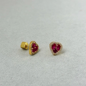 Detailansicht goldener Herzohrringe mit roten Rubinen und Zirkonia auf grauem Filzgrund