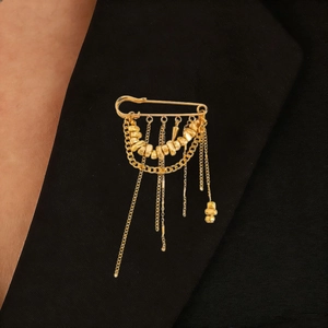Detail of a gold safety pin brooch with hanging fringe chains on a black blazer lapel