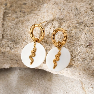 Macro view of gold-plated snake earrings with natural white shell charms on sand texture